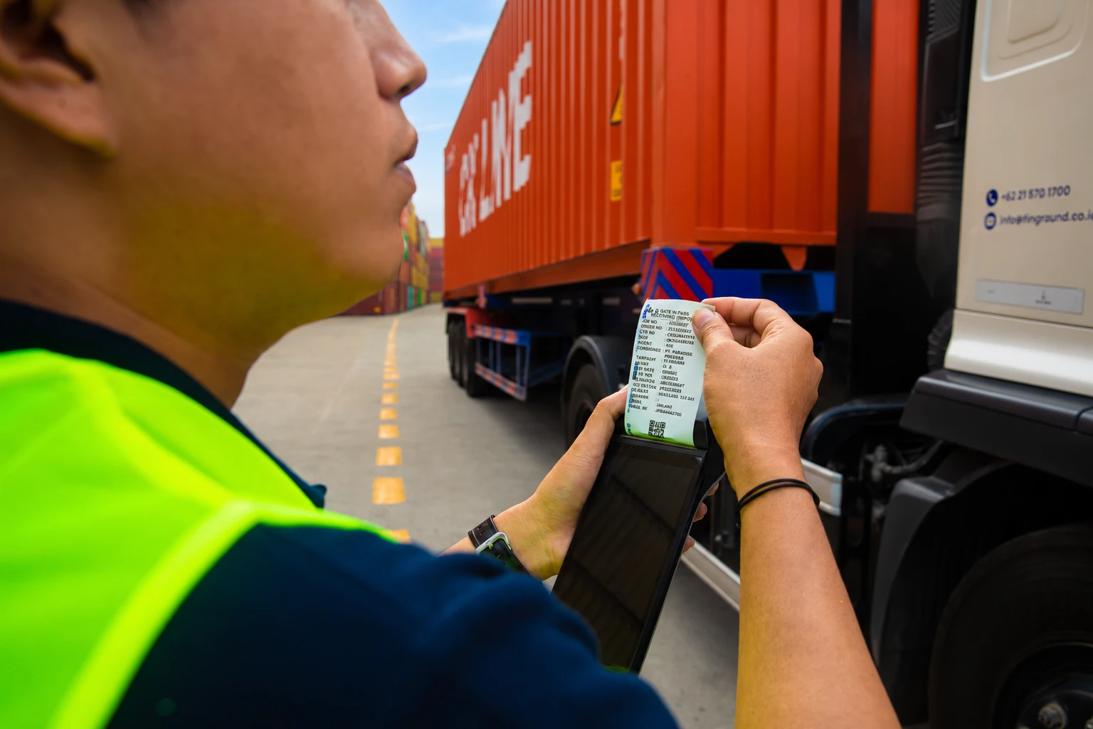 Officer checking a printed digital gate pass beside a container truck